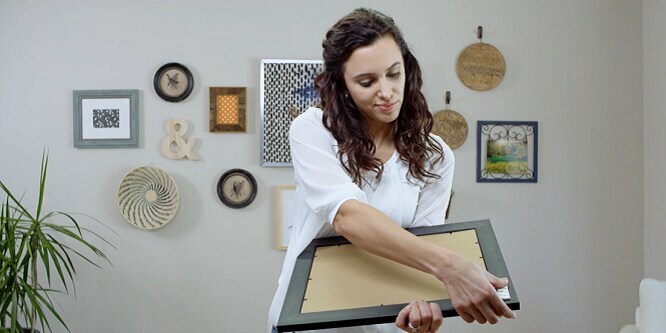 Woman showing how to apply Command™ Picture hanging Strips
